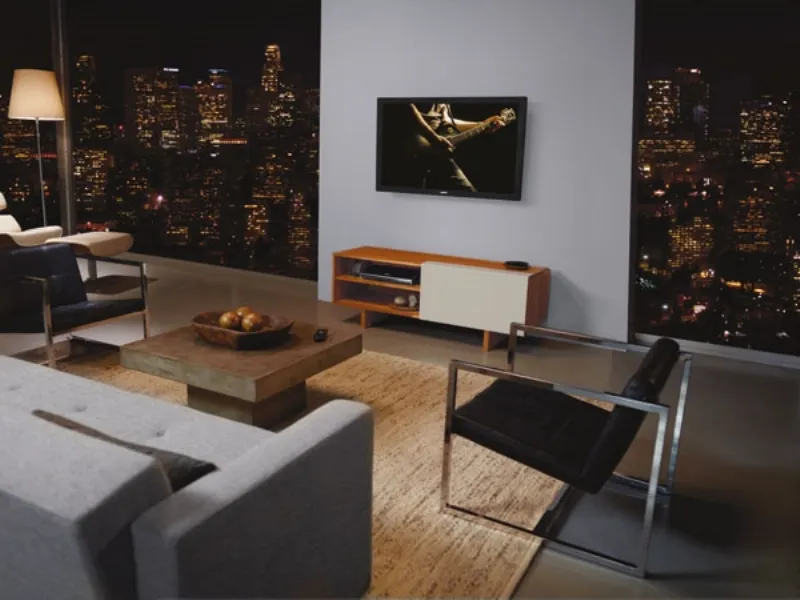 zona living con parete finestrata, tavolino in legno, sedie design nere con dettagli in acciaio, schermo tv a parete con chitarrista