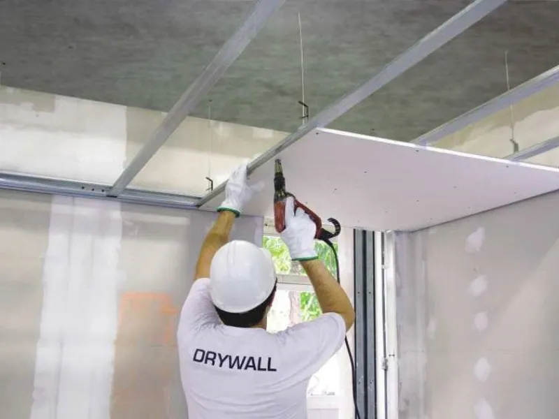 In questa foto è ritratto un operaio che fissa ai profili metallici un pannello di cartongesso: probabilmente, si tratta della realizzazione di un controsoffitto