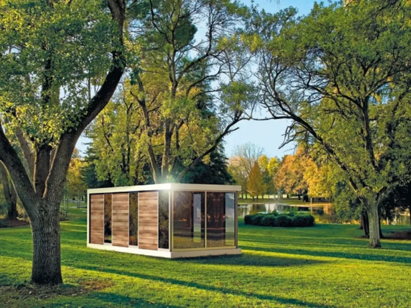 mobile abitativo in legno e vetro trasparente in prato con alberi e lago sullo sfondo
