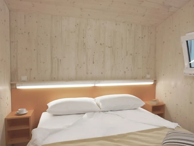 Letto matrimoniale con biancheria bianca e beige, neon e pareti in legno chiaro