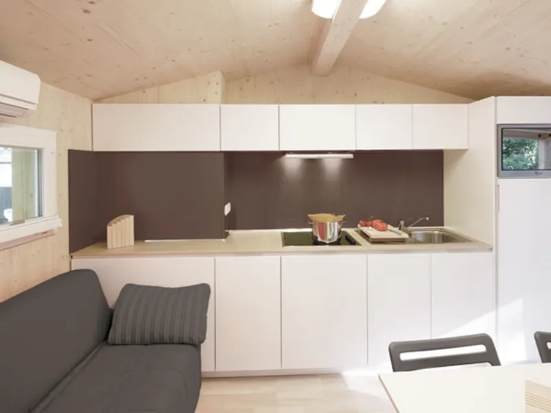 mobile cucina bianco panna con pannello muro marrone scuro, soffitto spiovente, pareti e pavimento on legno chiaro, divano antracite