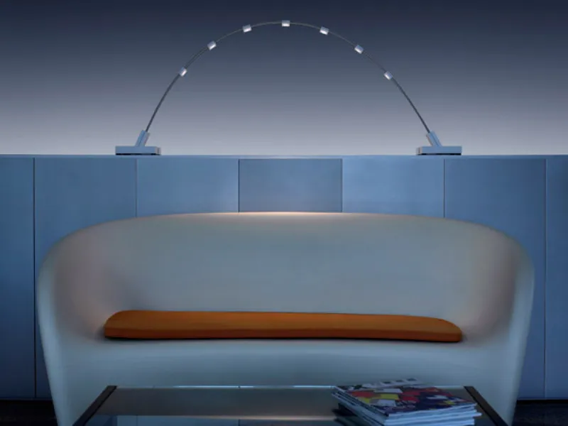 divano curvilineo bianco con seduta arancio, lampada da tavolo composta da due nastri d'acciaio ricurvi e punti luce