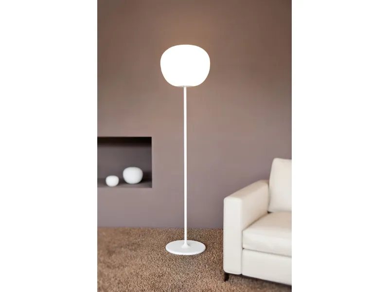 lampada da terra bianca con stelo verticale e paralume sferico, tappeto color naturale e poltrona bianca