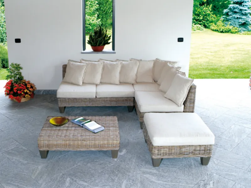 divano da esterno a quattro posti a L in rattan e cuscini panna, pouf in coordinato, tavolino basso in rattan.