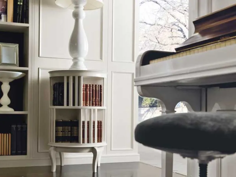 dettaglio boiserie e girello portalibri bianchi, abat-jour bianca e pianoforte in primo piano