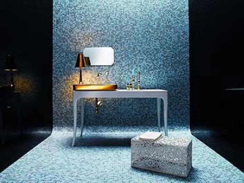 fascia di parete e pavimento a mosaico nelle tinte del blu con tavolino bianco, abat jour con lavabo dorati e puf in ferro battuto bianco