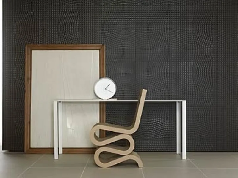 seduta design in gres porcellanato vista di profilo, cornice in legno appoggiata alla parete e tavolo bianco con orologio