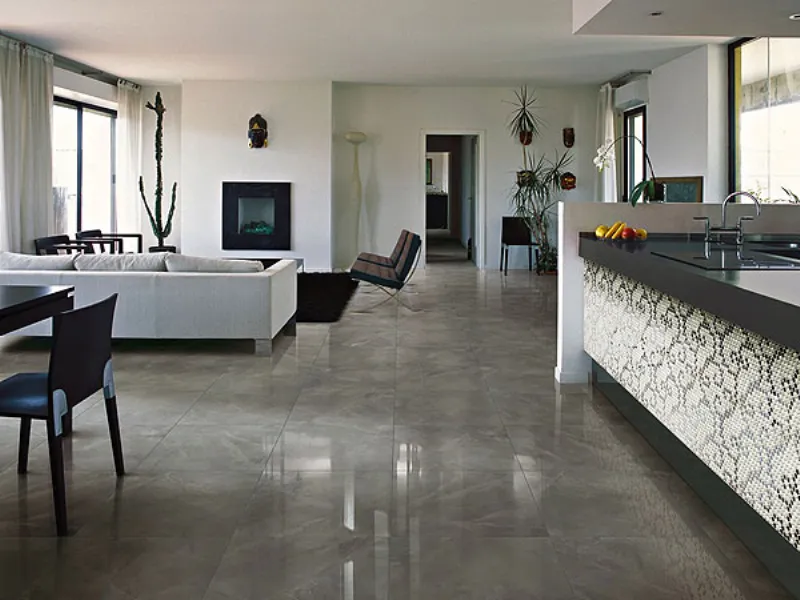 cucina e zona living con penisola con piano nero e parete rivestita a mosaico, pavimento a piastrelle di marmo, divano bianco e camino