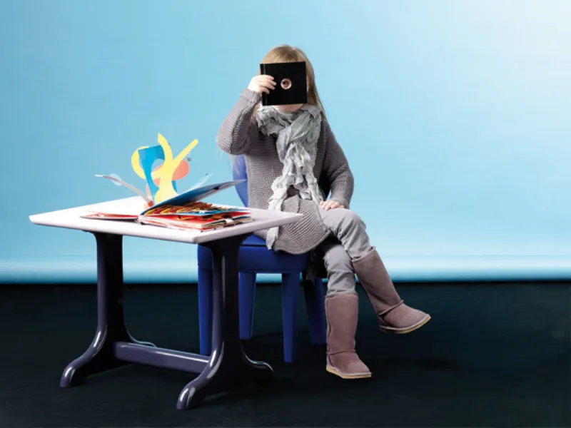 bambina seduta su sedia blu, tavolino con libro pop-up