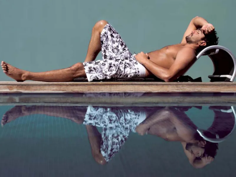 uomo in boxer con grafiche nere su sfondo bianco su bordo piscina su sedia Beachbuddy