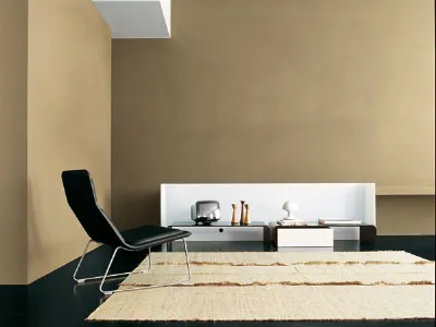 spazio living con parete beige, poltrona design nera, tappeto naturale e tavolini con spalliera bianca